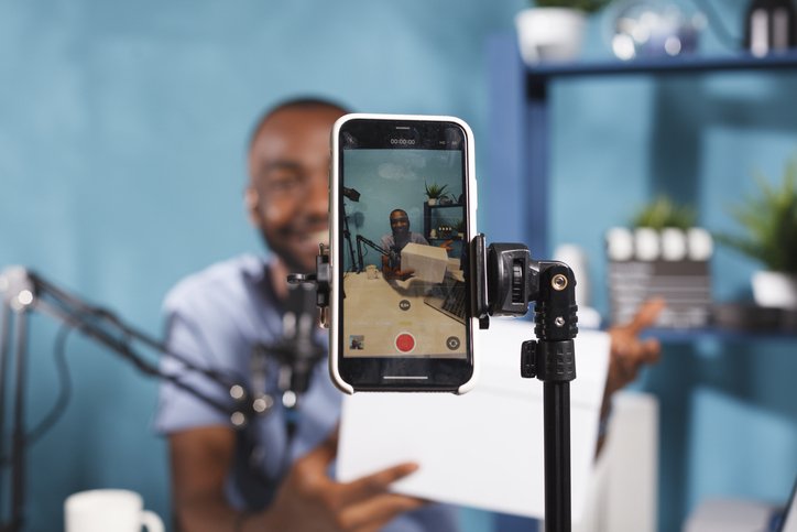 Foto de homem gravando um vídeo em celular posicionado em tripé.