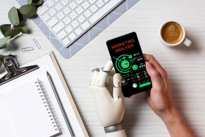 Foto de mão humana e mão robótica segurando um telefone com dados de análise de marketing.
