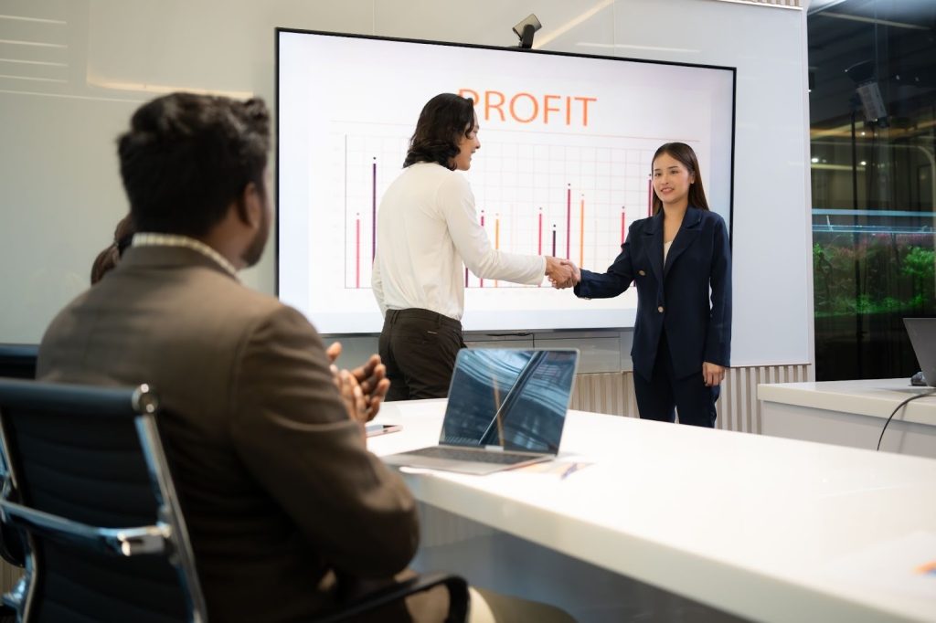 Foto de pessoas dando aperto de mão em frente a tela com lucros.